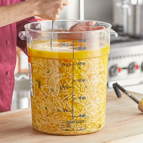 A man stirring food in a large Vigor food storage container on a counter.