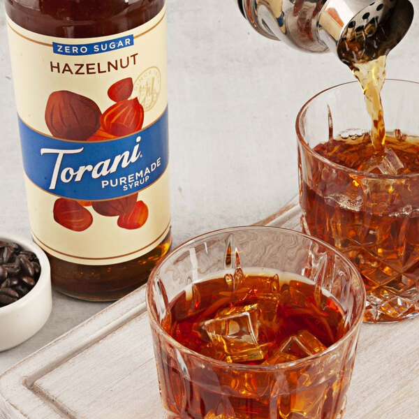A glass of hazelnut coffee being poured from a bottle of Torani Hazelnut Flavoring Syrup.
