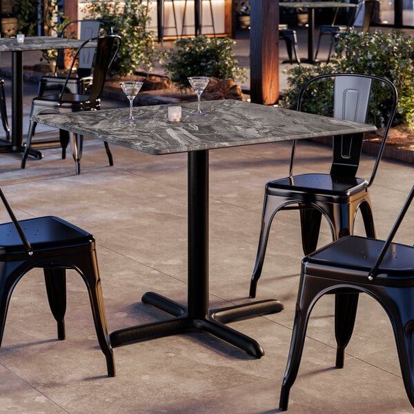A square table with a smooth Paladina finish and black metal base, surrounded by black metal chairs in an outdoor setting.