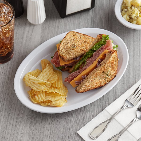 An Acopa white melamine oval platter with a sandwich and chips on a table.