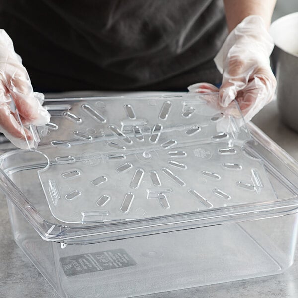 A person in gloves holding a Vigor clear polycarbonate drain tray over a counter.