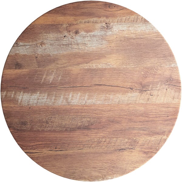 A Lancaster Table & Seating Excalibur round wood table top with a textured Yukon Oak finish and white lines in a circular pattern.