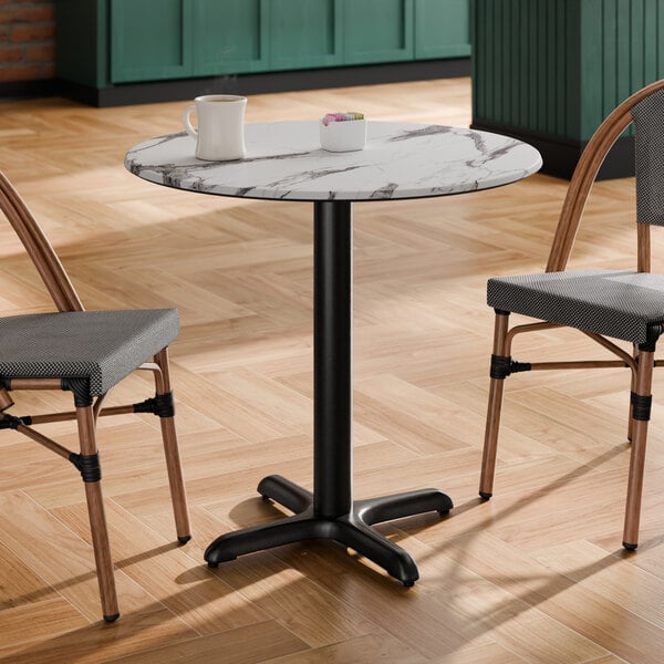 A round table with a smooth Versilla finish and a black pedestal base, shown with two chairs.