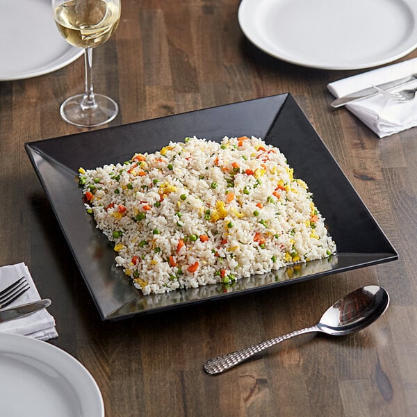 A plate of rice with vegetables on an Acopa Rittenhouse black square melamine plate.