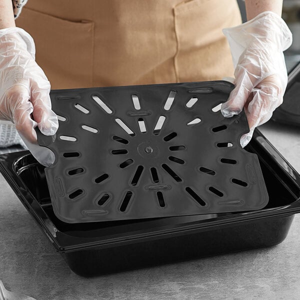 A person in gloves holding a black Vigor polycarbonate drain tray over a counter.