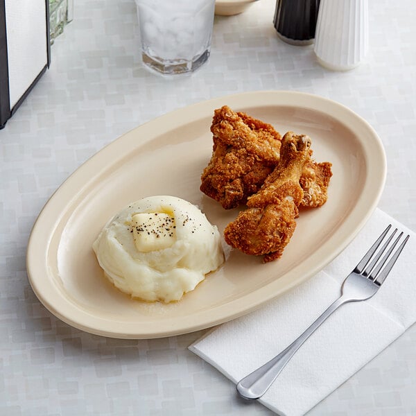 A tan Acopa Foundations narrow rim oval platter with mashed potatoes and chicken on a table.