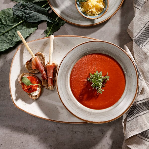 A beige porcelain coupe platter with a piece of bread and a slice of tomato with cheese on top.