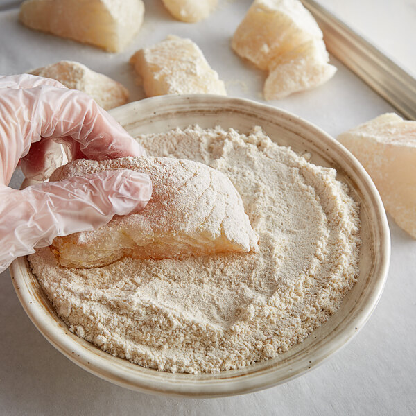 A person in gloves holding a bowl of J.O. Fish Fry in flour.