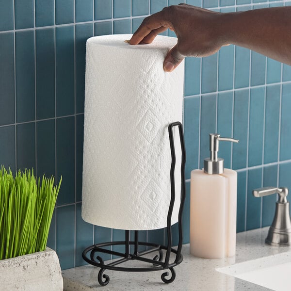 A wrought iron paper towel holder with a roll of paper towels placed on a kitchen or bathroom countertop.