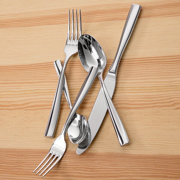 A group of Fortessa Lucca stainless steel dinner forks on a wood surface.