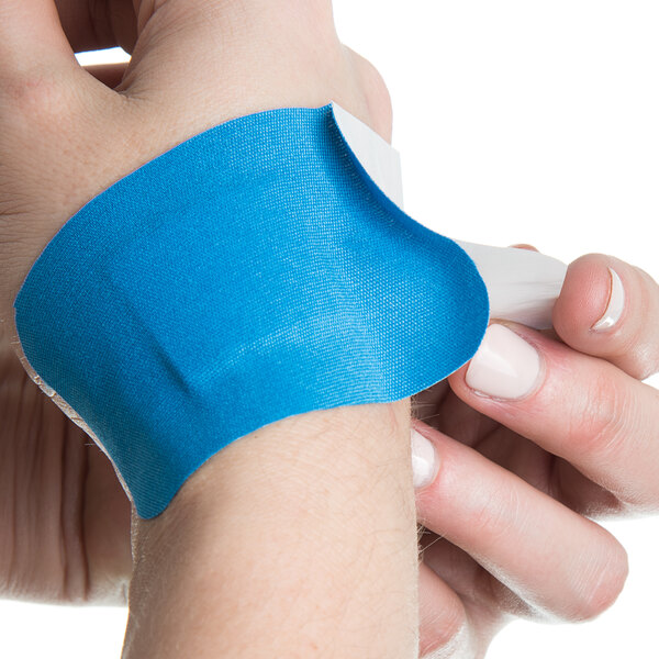 A person's hand with a blue San Jamar Mani-Kare bandage on their wrist.