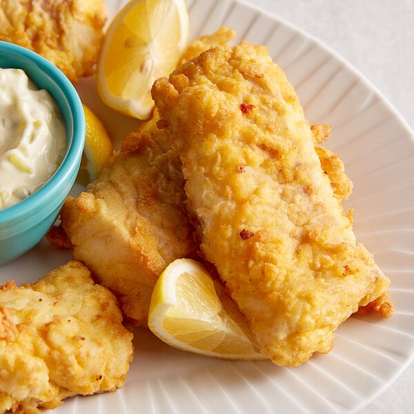 Fried fish on a plate with lemon wedges.