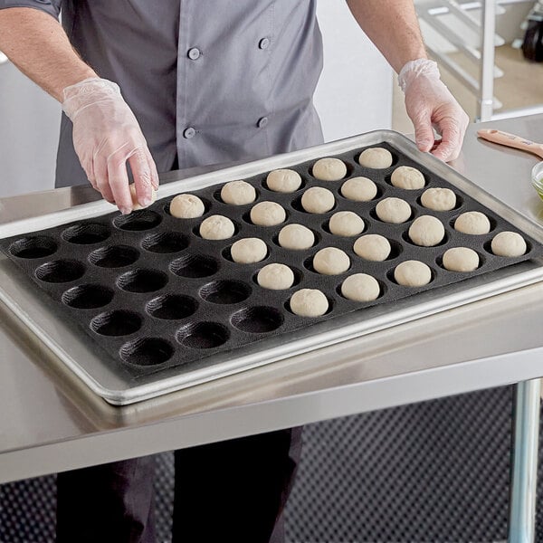 A person in a chef's uniform putting dough into a Sasa Demarle bread mold.