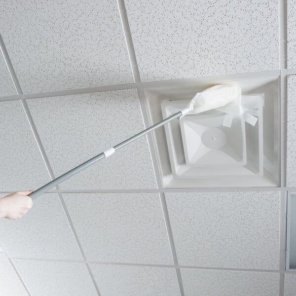 A hand using a Unger ProDuster on a white ceiling with a silver handle.