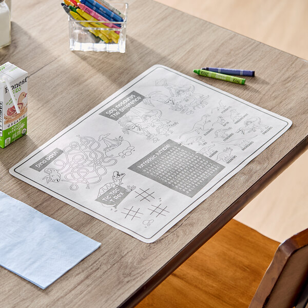 A kids' dinosaur-themed interactive placemat with games and activities, accompanied by a pack of four triangular crayons.