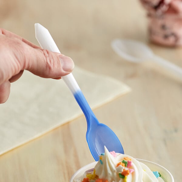 A hand holding a blue and white color-changing dessert spoon over a cup of ice cream.