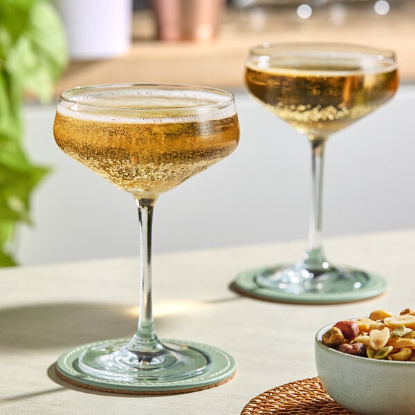 Two Schott Zwiesel coupe glasses filled with champagne on a table with a bowl of nuts.