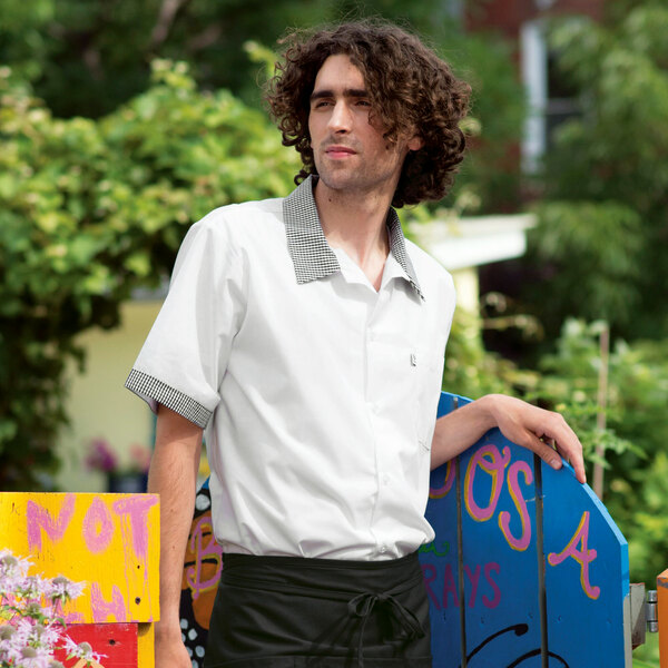 A man with curly hair wearing a white Uncommon Chef cook shirt with Shepherd's check trim.
