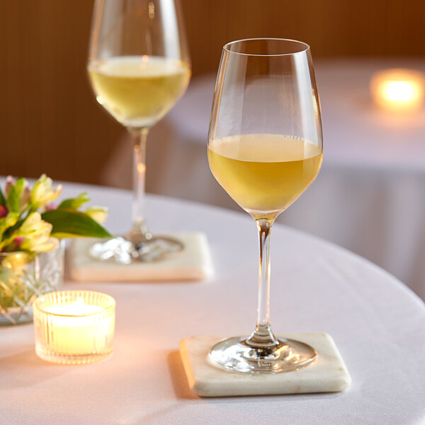 Two Schott Zwiesel Forte white wine glasses on a table with a candlelit centerpiece.