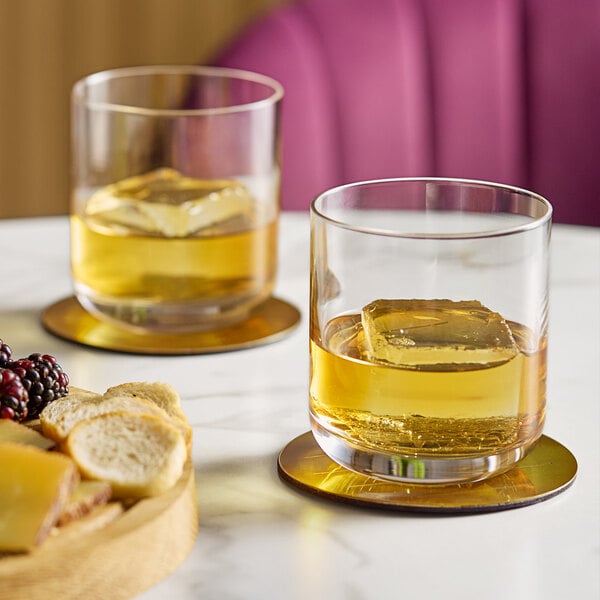 Two Schott Zwiesel old fashioned glasses of whiskey on a coaster.