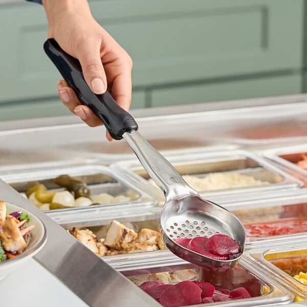 A hand using a Vollrath black Perforated Oval Spoodle to serve food at a salad bar.