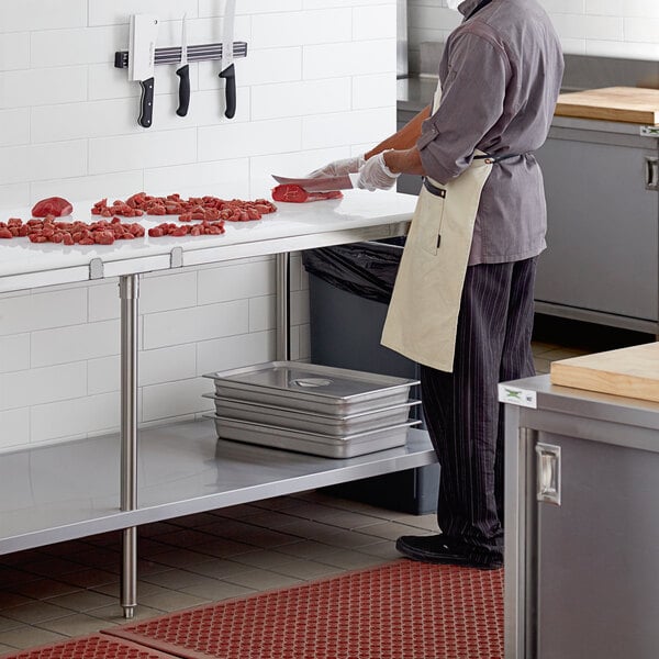 A man cutting meat on a Regency stainless steel poly top table.