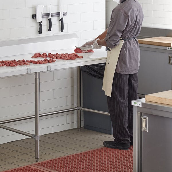 A man cutting meat on a Regency stainless steel poly top table.