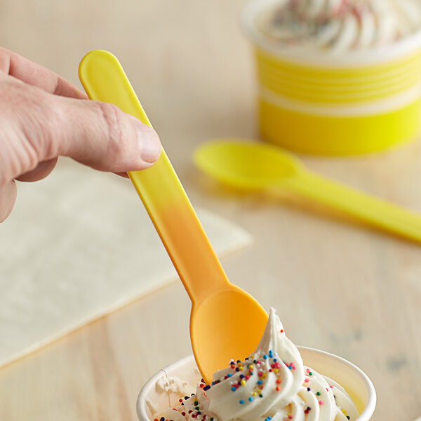 A hand holding a yellow spoon over a cup of frozen yogurt.