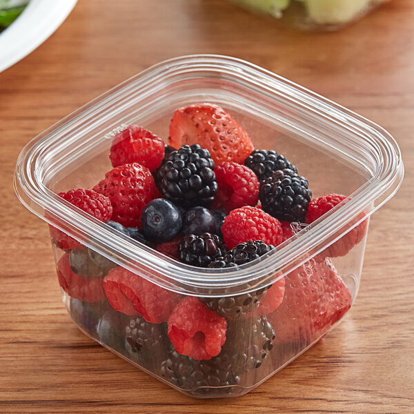 A plastic container of berries with a Fabri-Kal LSQ TruWare Square Plug Fit PET Deli Lid on a table.