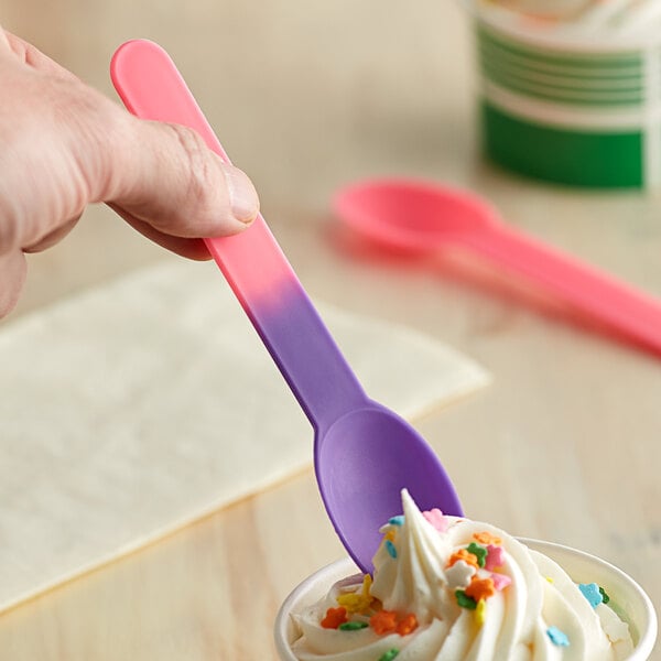 A hand holding a pink and purple color-changing heavy weight plastic spoon over a cup of ice cream.