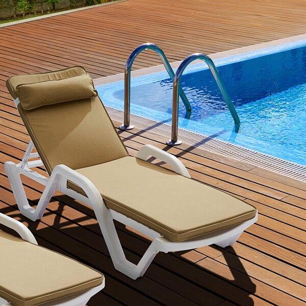 A Lancaster Table & Seating beige chaise cushion on a chaise lounge chair next to a swimming pool.