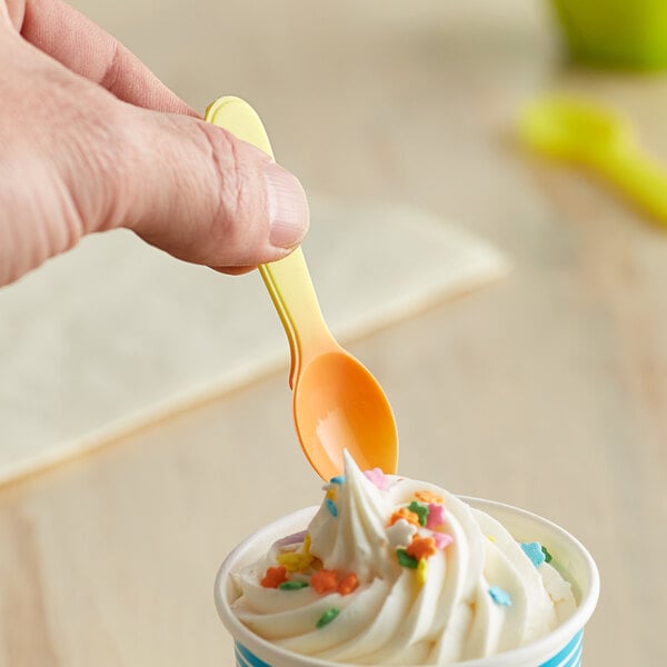 A hand holding a yellow color-changing tasting spoon over a cup of white dessert