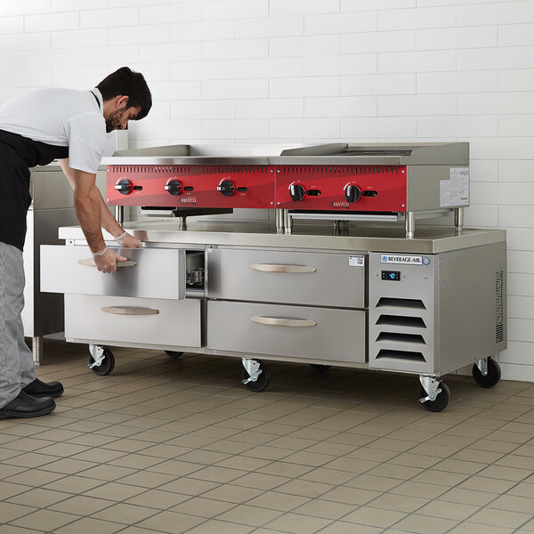 A man in a white shirt and black apron using a Beverage-Air 4 drawer freezer chef base as a counter.