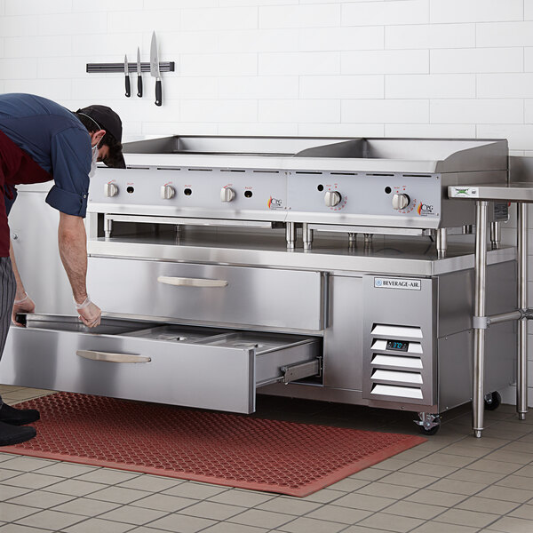 A man using a Beverage-Air 2 drawer refrigerated chef base with a flat top in a professional kitchen.