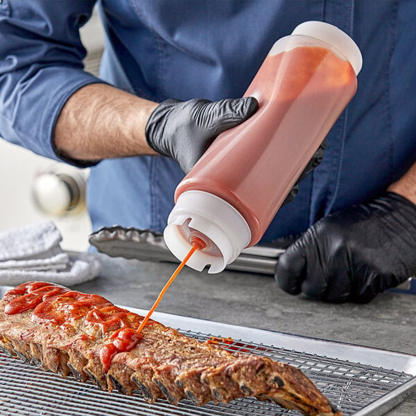 A person pouring sauce onto a rack of ribs using a Tablecraft squeeze bottle.