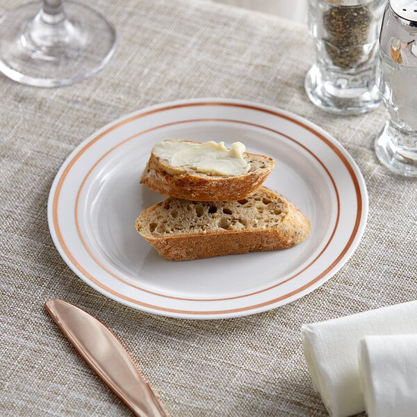 A white plastic plate with rose gold or copper bands, holding two pieces of bread, one with butter.