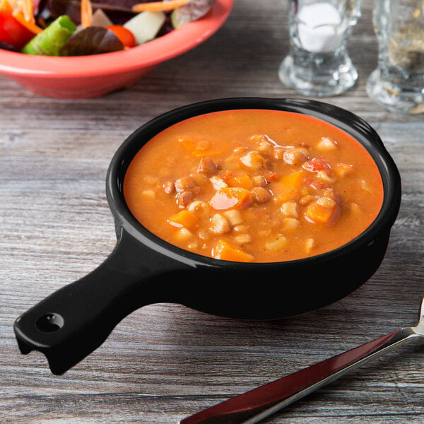 A black Elegance bowl filled with soup on a table.