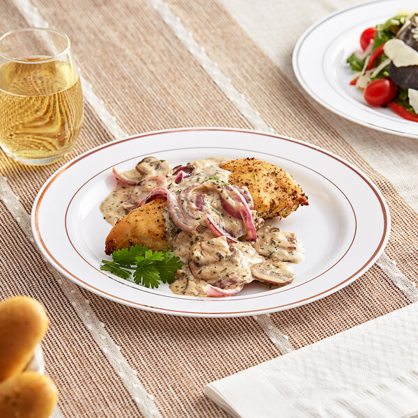 A Visions white plastic plate with rose gold bands holding a plate of food on a table.