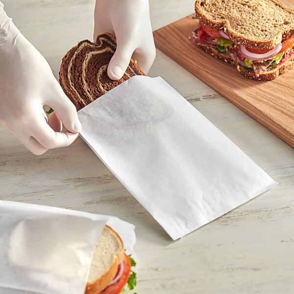 A person in gloves putting a sandwich in a white Choice sandwich bag.