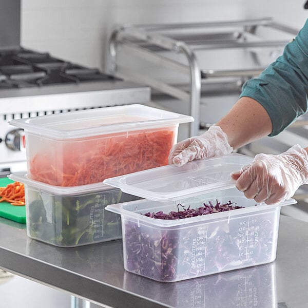 A woman wearing gloves and a green shirt using a San Jamar ModPan plastic container to hold purple shredded cabbage.