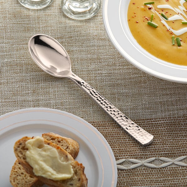 A Visions rose gold plastic spoon on a plate of soup.