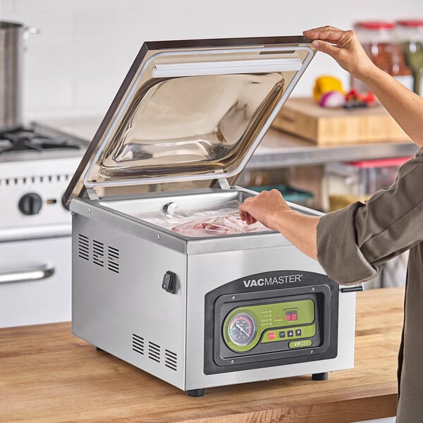 A person using an ARY VacMaster VP220 vacuum packaging machine on a counter.