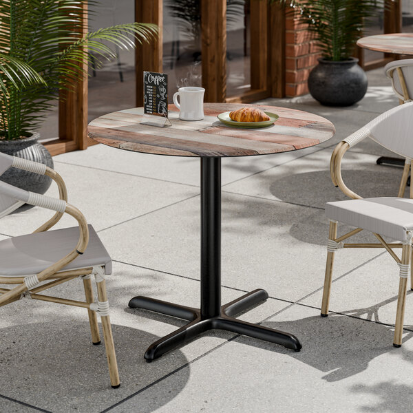 A round table with a textured mixed plank finish and a black pedestal base.
