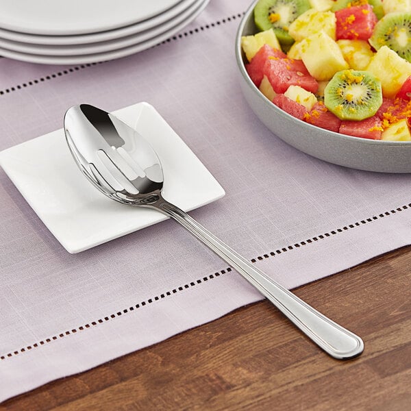 A spoon with a slotted bowl on a plate of fruit salad.