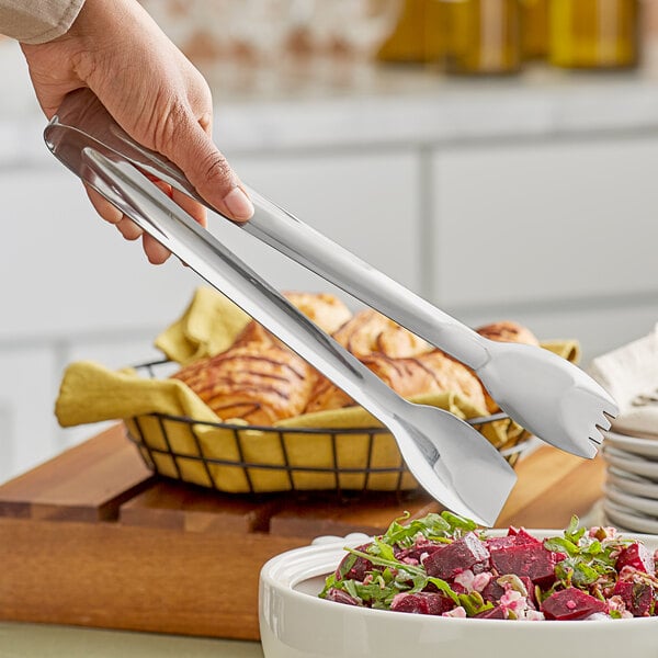 A person using GET stainless steel tongs to serve food from a bowl.