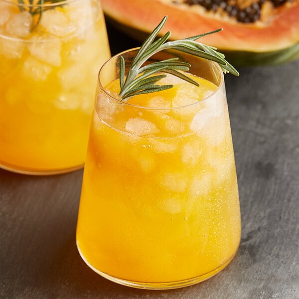 A glass of orange liquid with ice and a sprig of rosemary next to another glass of the same.