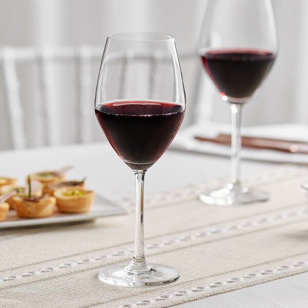 Two Acopa wine glasses filled with red wine on a table.