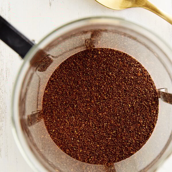 A glass jar filled with Crown Beverages Emperor's Finest Coarse Ground Coffee with a spoon.