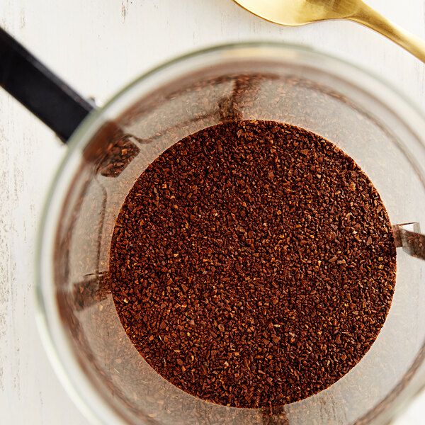 A glass jar of Crown Beverages Emperor's Finest Decaf Coarse Ground Coffee with a spoon.