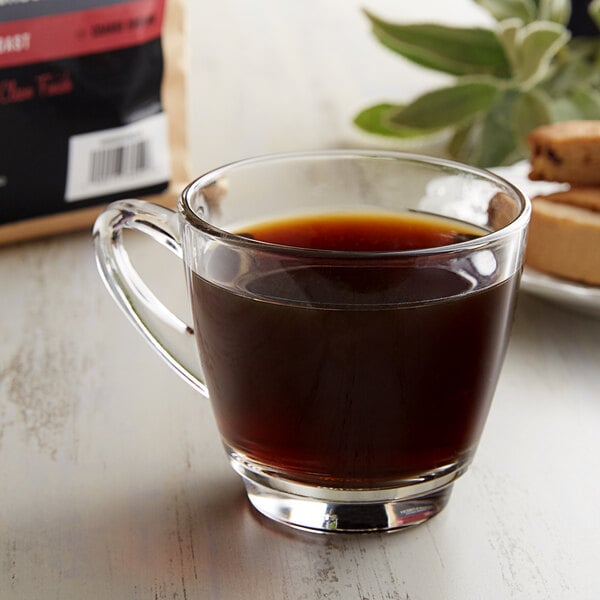 A glass cup of coffee with a bag of Crown Beverages Emperor's Finest Decaf Coarse Ground Coffee.